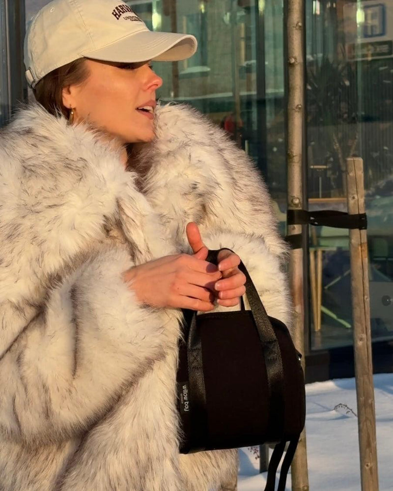 Woman in a fur coat and cap holding a black Vogue Mini Neoprene Day Bag with top handles.