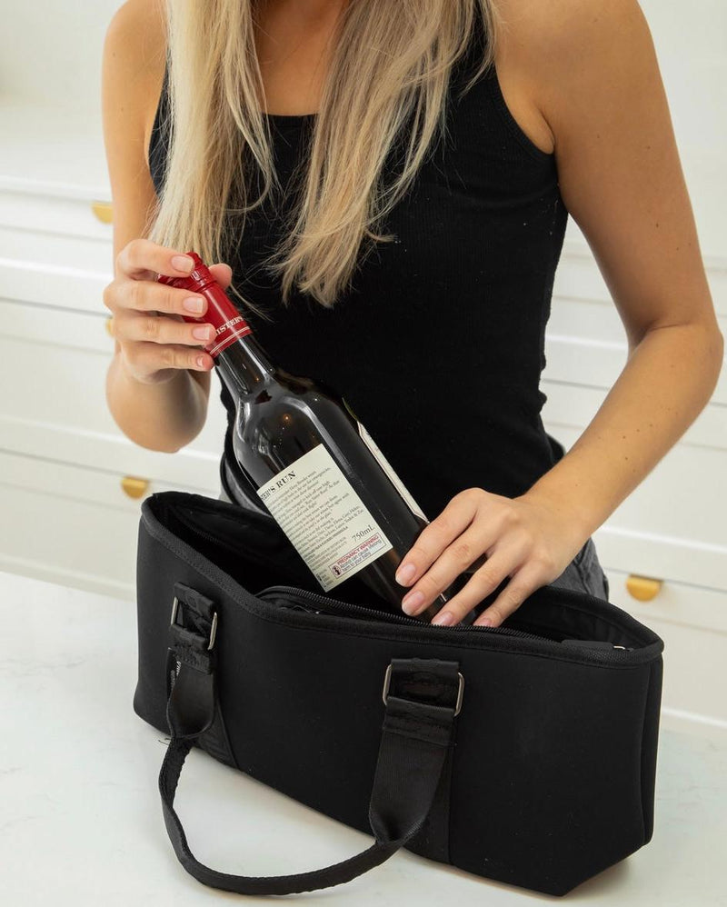Woman placing a red wine bottle into a black neoprene insulated wine carry bag.